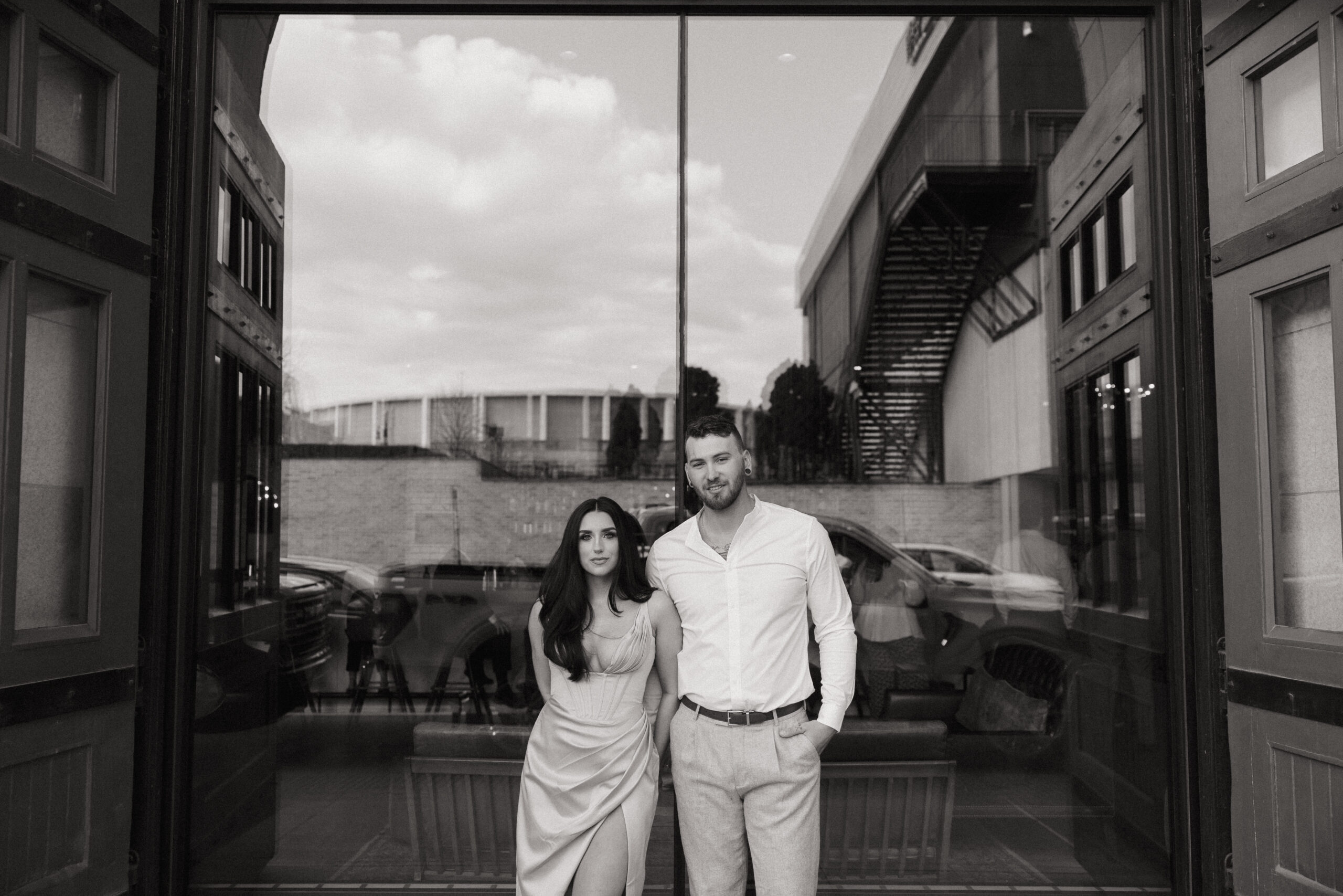 Detroit Engagement Photographer Downtown City cocktails luxury Black and white photo of guy and girl holding hands behind her back, both looking at camera